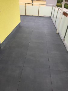 Dunkle Verfliesung eines Balkons mit Geländer